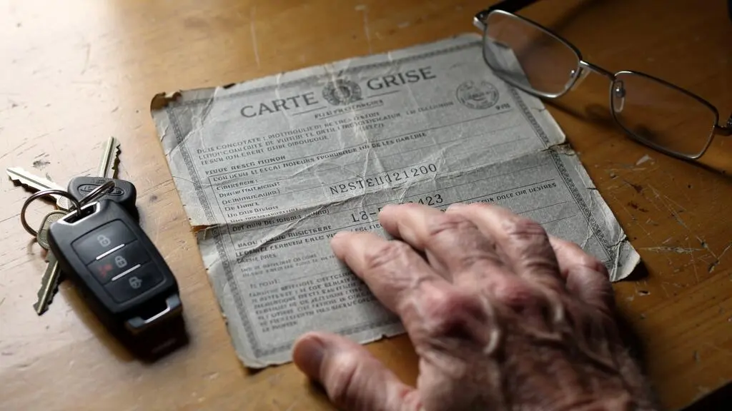 Une carte grise ancienne posée sur un bureau avec des clés de voiture.